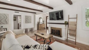 Un salon moderne avec un canapé, une table basse, une cheminée, un téléviseur et des poutres en bois au plafond.