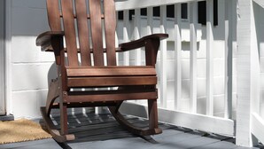 A wooden rocking chair on a porch with a white fence.