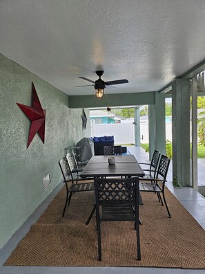 Ein überdachter Patio-Bereich mit Tisch und Stühlen, einem Deckenventilator und einer roten Stern-Dekoration an der Wand.