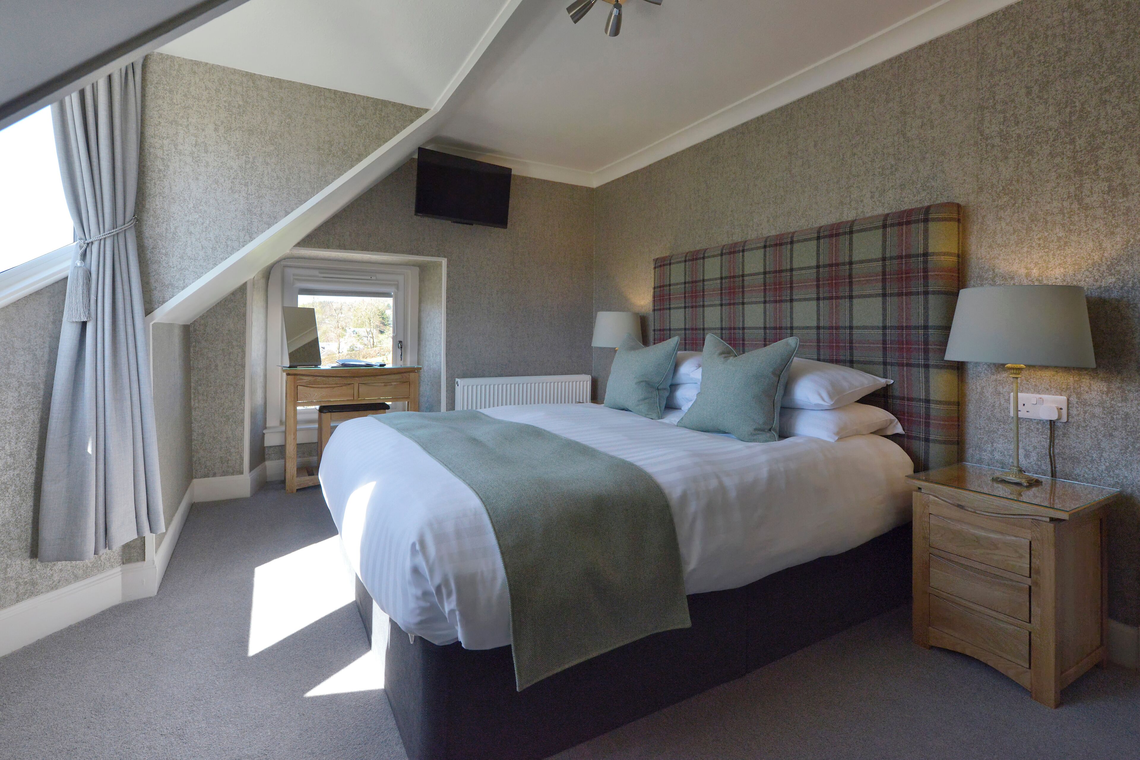 A bedroom with a bed, bedside tables, a TV, a window with curtains, and a plaid headboard.