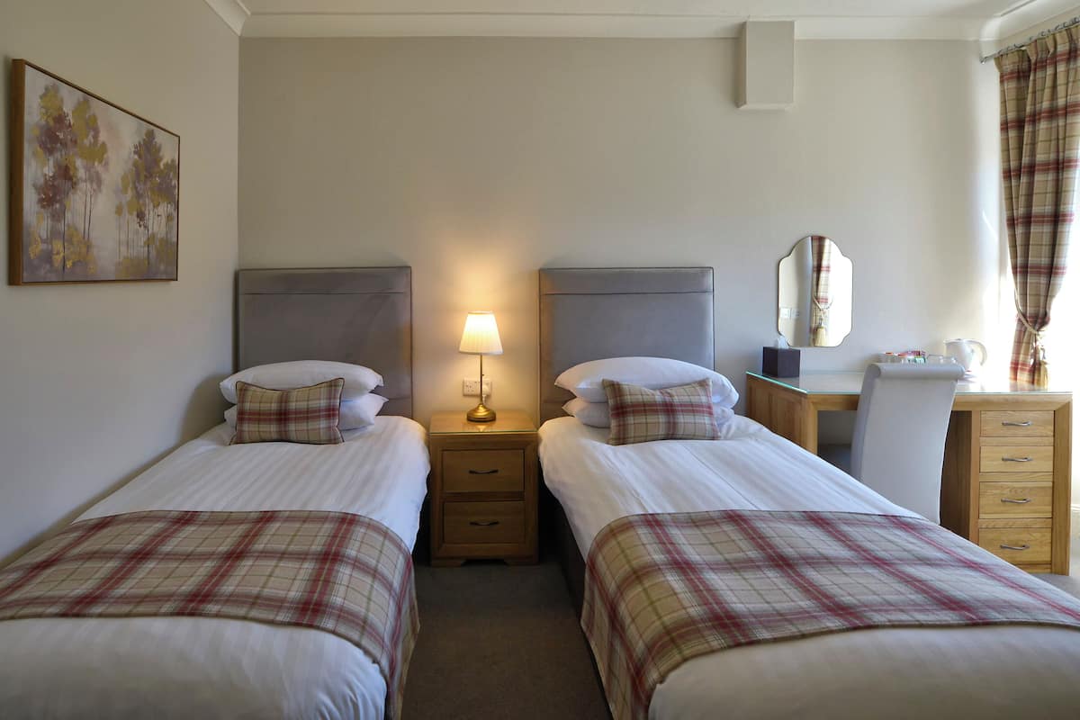 A hotel room with two beds, a desk, a chair, a lamp, a mirror, and a dresser.