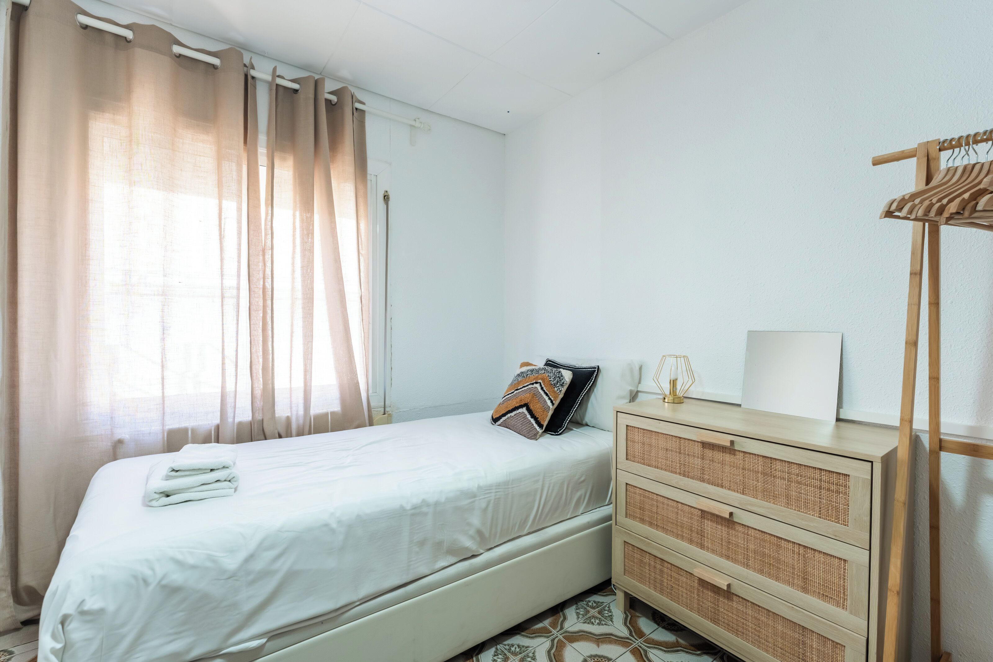 Une chambre à coucher bien rangée, avec un lit, une commode et un porte-vêtements en bois.