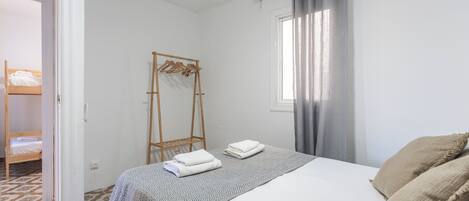 Un dormitorio con una cama, un armario de madera, un tendedero y una ventana con cortinas.