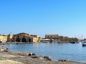 Un pueblo costero con edificios históricos de piedra, un puerto deportivo con barcos y un litoral rocoso.