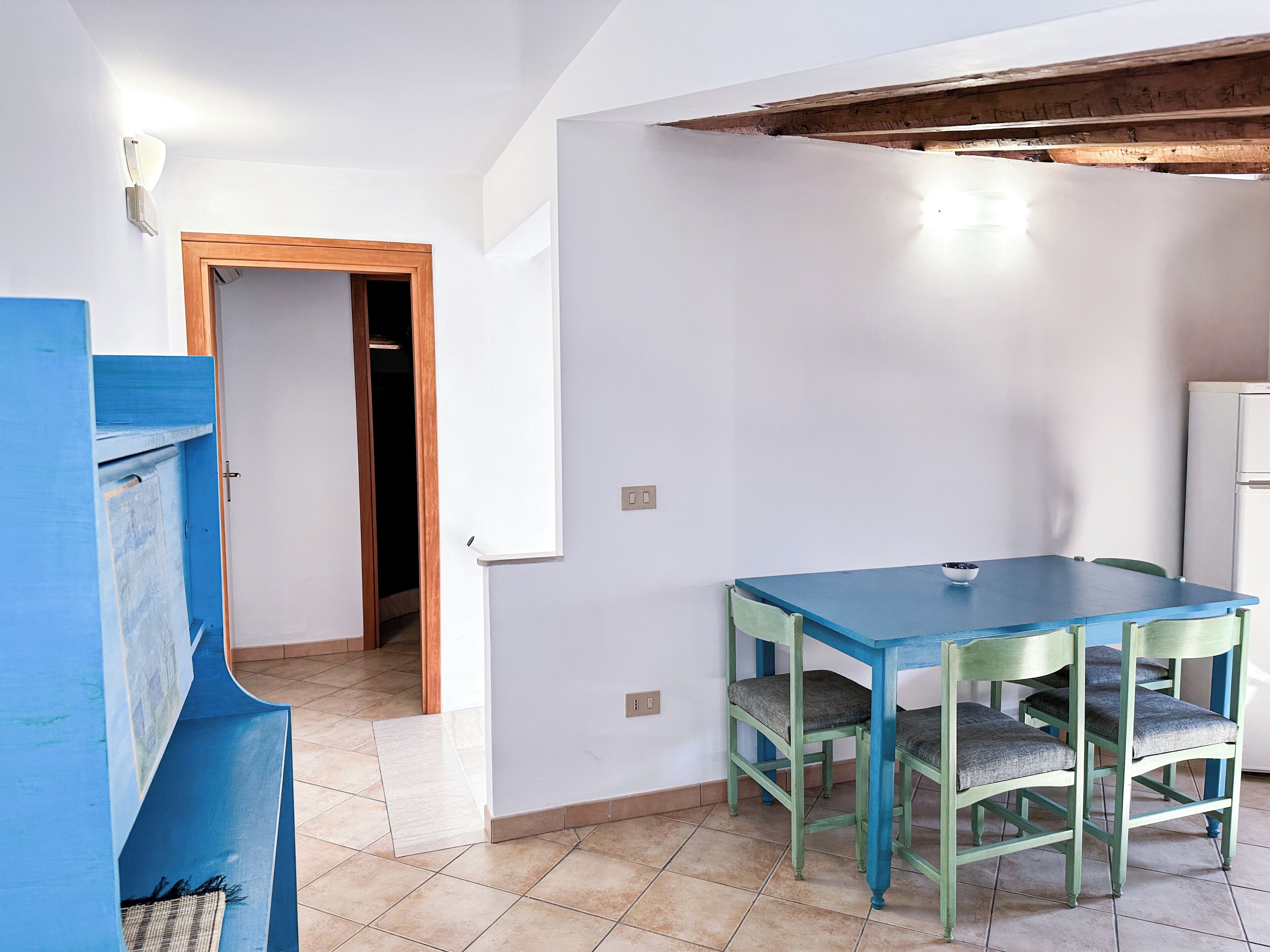 A room with a blue table and green chairs, a wooden door, and a white wall.