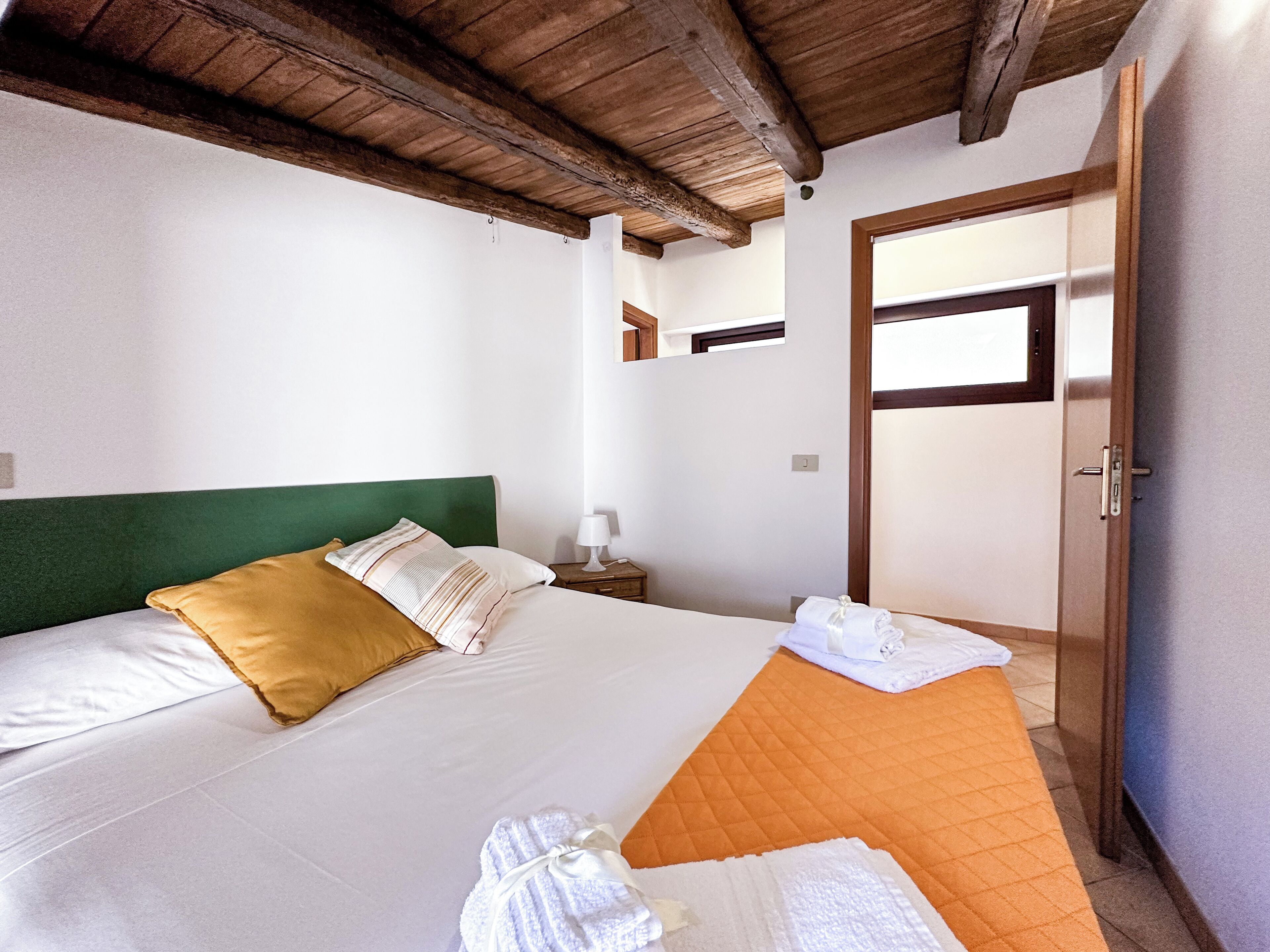 Un dormitorio con cama, almohadas, mesita de noche, lámpara y puerta.