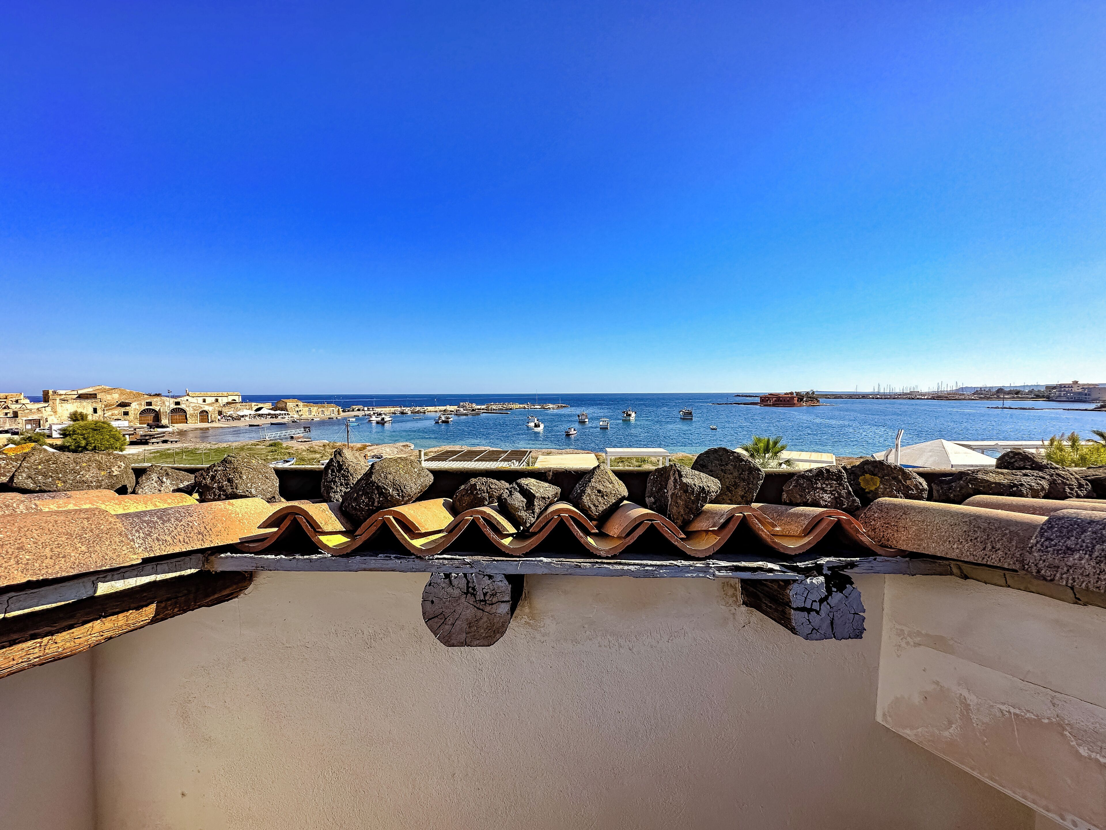 A coastal view with a clear sky, rocky terrain, and a harbor with boats.