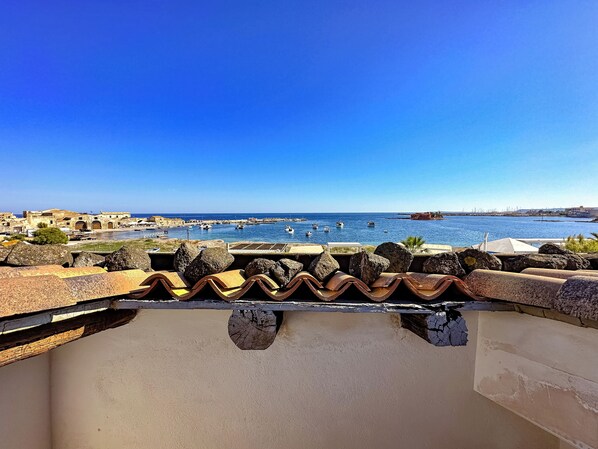 Vista costera con cielo despejado, terreno rocoso y un puerto con barcos.
