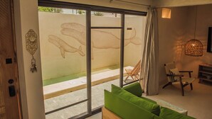A modern living room with a sliding glass door leading to a patio. There is a green sofa, a wooden chair, and a hanging light fixture. - Manglito Manila, a 3 Minutos del Malecón de La Paz (La Paz)