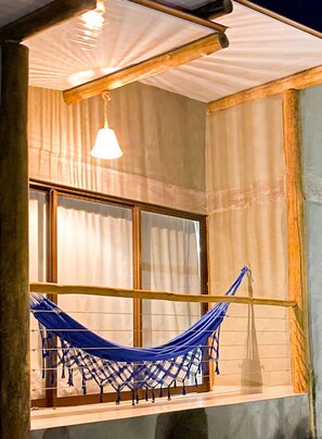 A hammock on a balcony with a window and a hanging light fixture.