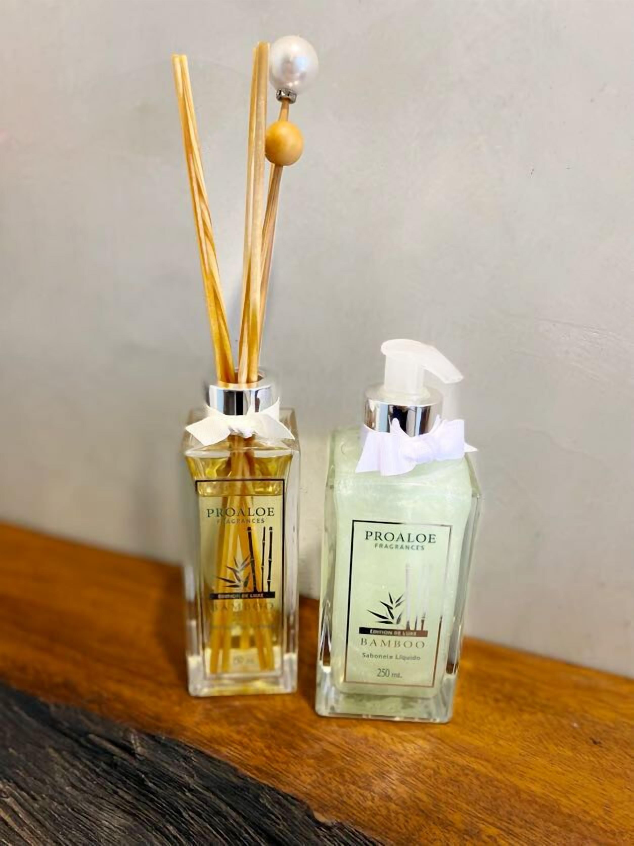 Two Proaloe fragrances bottles, one with reed diffusers and one with a pump dispenser, on a wooden surface.