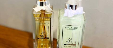 Two Proaloe fragrances bottles, one with reed diffusers and one with a pump dispenser, on a wooden surface.
