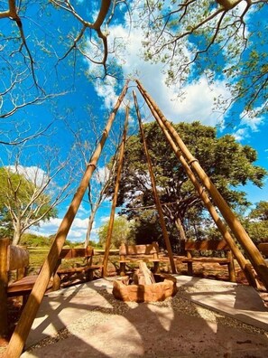 A traditional wooden structure with a thatched roof, surrounded by trees and a clear sky. - Sítio Rio Gouveia (Brotas)