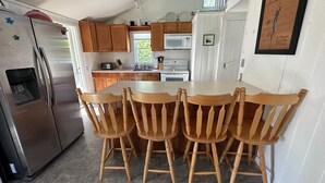 Una cocina con armarios de madera, un refrigerador de acero inoxidable, un microondas y una mesa de comedor con sillas de madera.