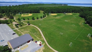 Vista aérea de un complejo deportivo con varias canchas, un estacionamiento y un edificio con techo rojo.