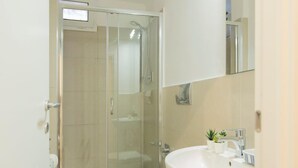 A modern bathroom with a glass shower enclosure, a white toilet, and a sink with a mirror. - Nina   Tiny Suite in Trastevere (ROMA)