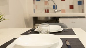 A clean, modern kitchen with white cabinets, a tiled backsplash, and a dining area set with plates, glasses, and cutlery. - Nina   Tiny Suite in Trastevere (ROMA)