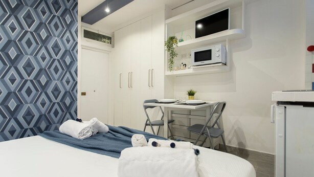 A hotel room with a bed, a desk, a microwave, and a small refrigerator. - Nina   Tiny Suite in Trastevere (ROMA)