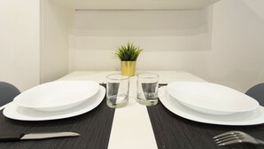 A dining table with two white plates, two clear glasses, a knife, and a fork. There is a small potted plant on the table. - Nina   Tiny Suite in Trastevere (ROMA)