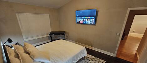 A bedroom with a bed, a TV mounted on the wall, a bedside table, and a patterned rug.