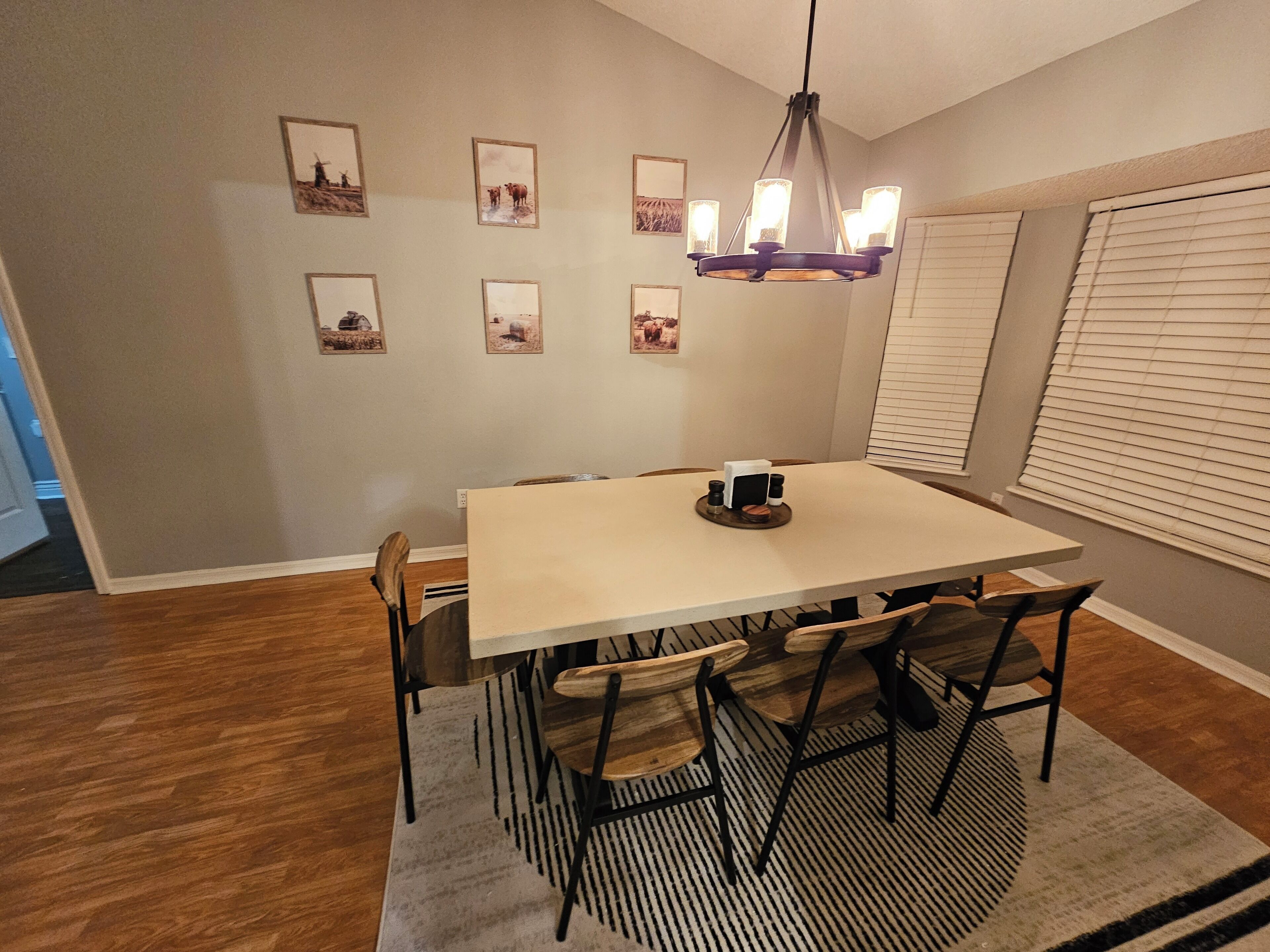 A dining area with a rectangular table, six chairs, a chandelier, and framed pictures on the wall.