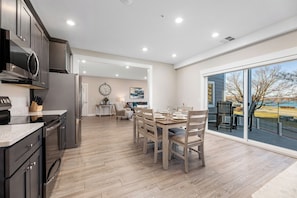A modern kitchen with stainless steel appliances, a dining area with wooden chairs, and a large sliding glass door to the outdoors. - 539 Bay St. Lake View Condo Unit 204E (Traverse City)