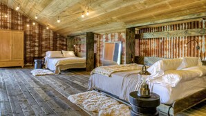 Een rustieke slaapkamer met houten vloeren en muren, twee bedden met witte lakens, een houten garderobe en een lamp in vintage-stijl.