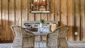 Een houten wand met een spiegel en lichtjes, een rieten bank met kussens, en twee rieten stoelen.