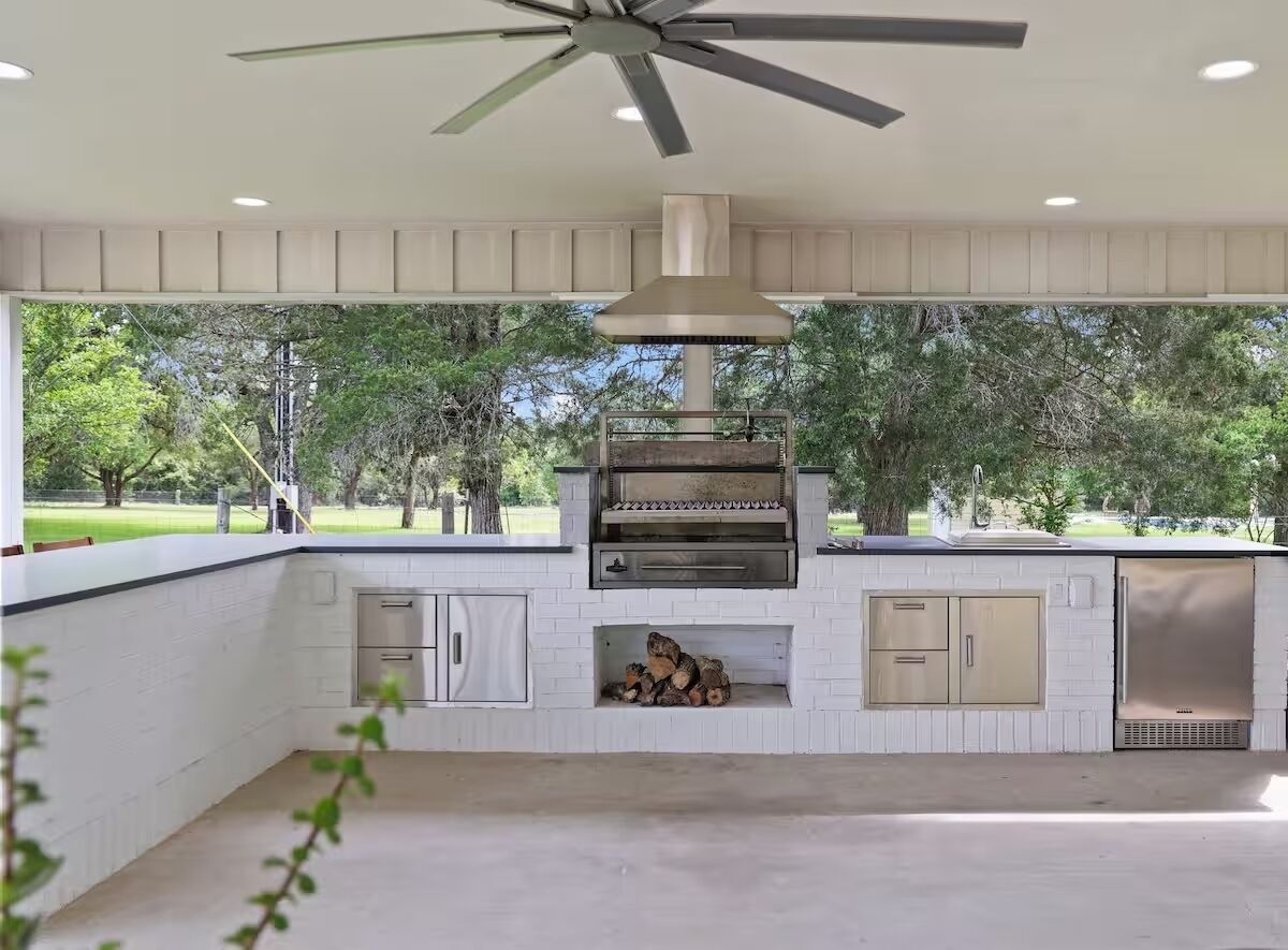 Una cocina exterior con una parrilla empotrada, un ventilador de techo y vistas a un parque.