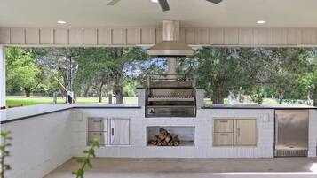 Una cocina exterior con una parrilla empotrada, un ventilador de techo y vistas a un parque.