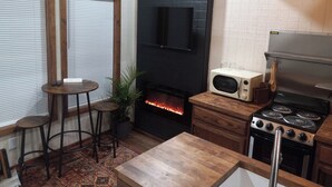 A kitchen with a wood stove, a microwave, and a stove. There is a small table and a plant. - Lil' Retreat on Poorhouse  (Starkville)