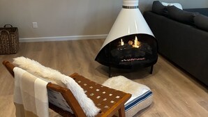 Un salon chaleureux avec un banc en bois, un plaid blanc et moelleux et une cheminée moderne.