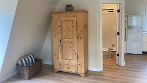 Un meuble en bois avec un panier et des coussins, un réfrigérateur blanc et un coin cuisine avec une porte blanche.