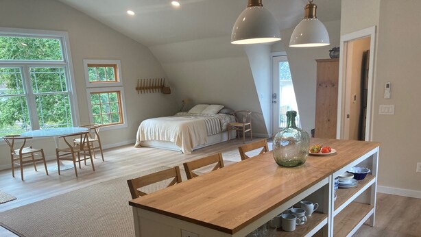 Une chambre spacieuse de style loft, dotée d’un grand lit, d’un coin repas avec une table en bois et d’une cuisine avec un plan de travail en bois.