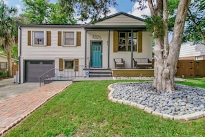 A two-story house with a garage, a front porch with a bench, and a tree in the front yard.