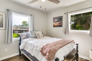 A bedroom with a bed, a ceiling fan, a window with curtains, and a painting on the wall.