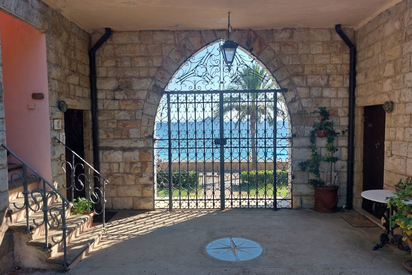 A stone-walled room with a large arched window overlooking a beach.