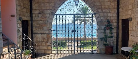 A stone-walled room with a large arched window overlooking a beach.