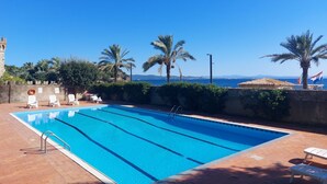 Una piscina con agua azul cristalina, rodeada de palmeras y vista al mar.