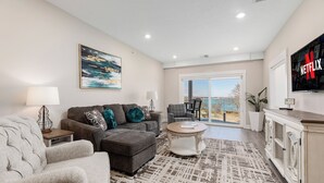 A living room with a sofa, armchair, coffee table, and a TV displaying the Netflix logo. - 539 Bay St. Lake View Condo Unit 302W (Traverse City)