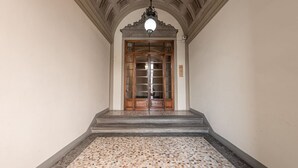 A hallway with a tiled floor, a wooden door with glass panels, and a decorative ceiling.
