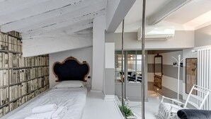 A modern bedroom with a large bed, a headboard, a bookshelf, and a bathroom visible through a glass partition.