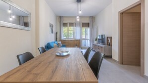 Un comedor con mesa de madera, sillas, un espejo, una lámpara en el techo y vistas a una ventana con cortinas.
