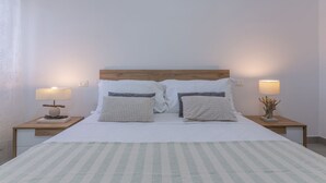 Una cama doble con dos almohadas, una mesita de noche con lámpara y otra mesita con lámpara.