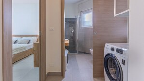 Habitación de hotel compacta con cama, lavadora y zona de ducha.