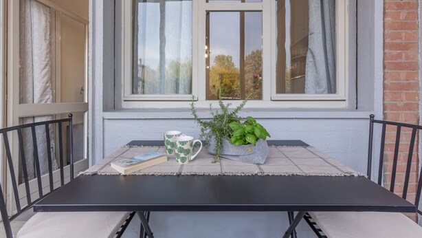 Una mesa con un libro, dos tazas y una planta en maceta sobre un mantel a cuadros.