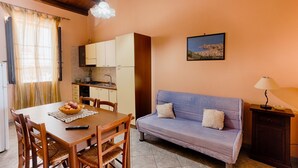 A cozy living area with a dining table, wooden chairs, a sofa, and a kitchen in the background.