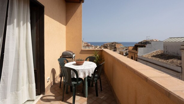 A balcony with a table and chairs, a grill, and a potted plant.