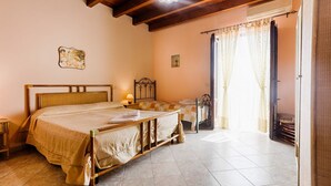 A bedroom with a wooden bed, a bedside table, a lamp, a window with curtains, and a small table with a chair.