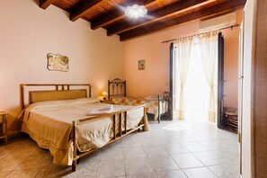 A bedroom with a wooden bed, a bedside table, a lamp, a window with curtains, and a small table with a chair.